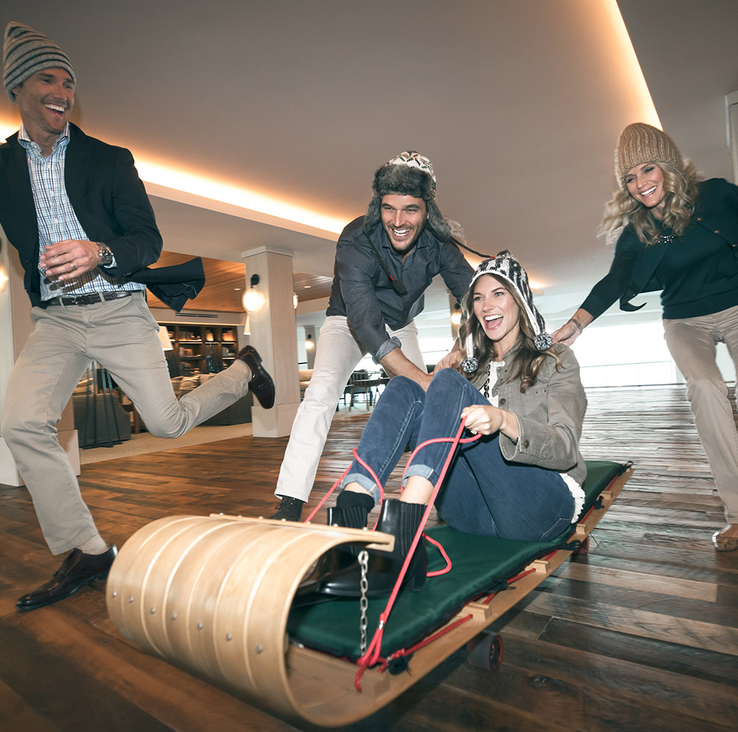 Group of adult friends decked out in winter clothing using a wooden tobaggan in the lobby