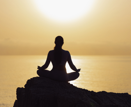 Silhouette of a woman meditating on a rock