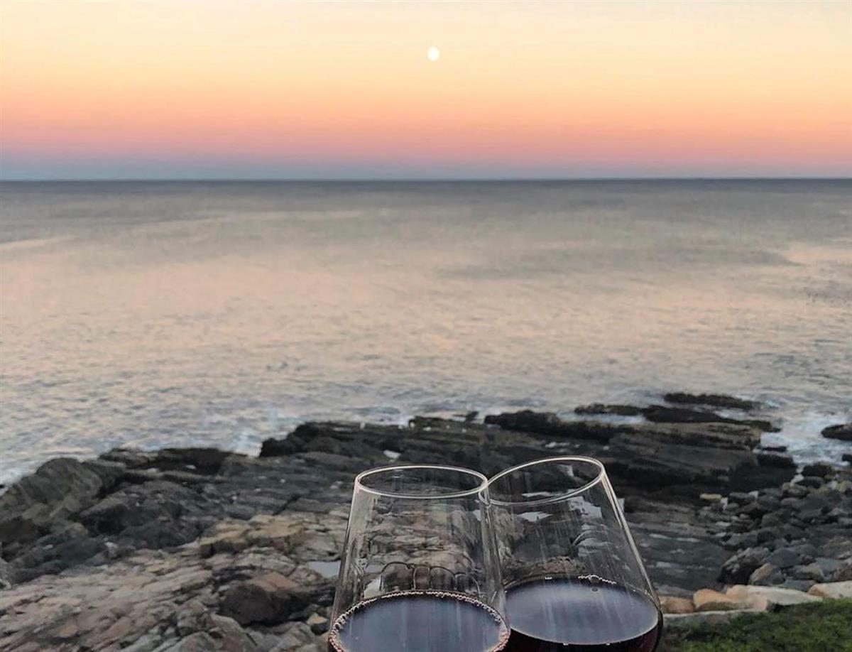 Two glasses clinking together for a cheers at sunset by the rocky shore